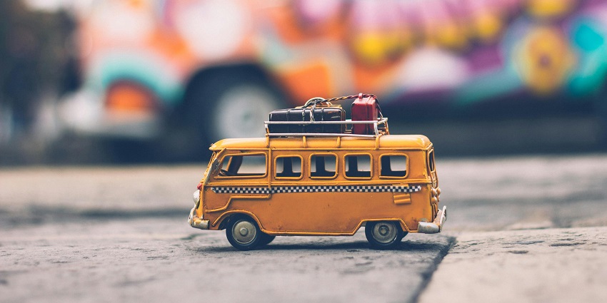 A unique view of a miniature yellow bus with luggage on the top standing on a road.