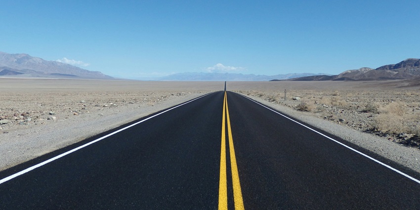 A daytime view of a road leading up to mountains surrounded by deserted pieces of land.