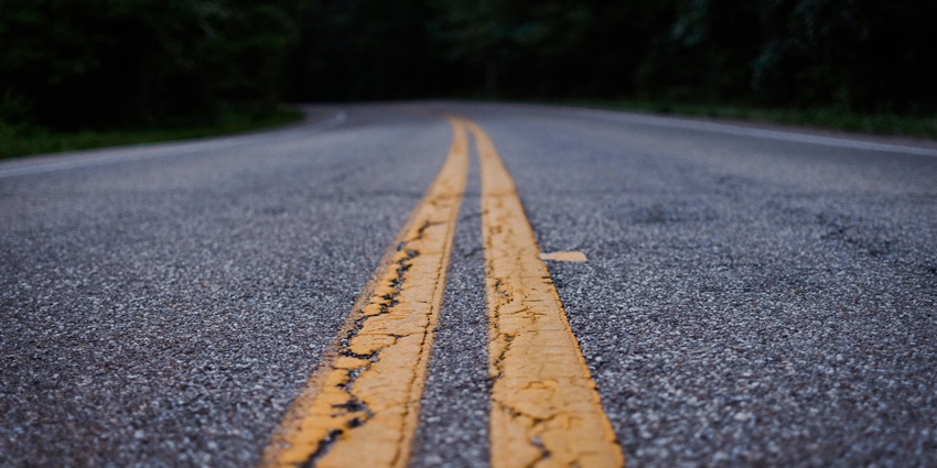 An enchanting view of a grey road with two yellow strips leading up to darkness.