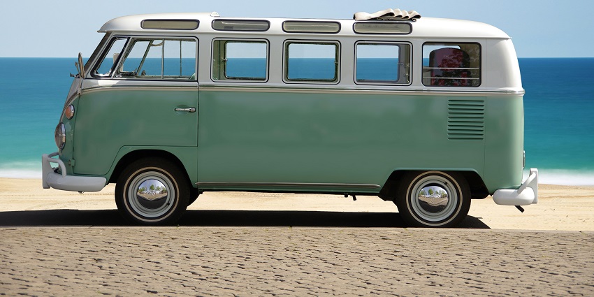 A daytime landscape of a green and white van standing on the side of an ocean on sand.