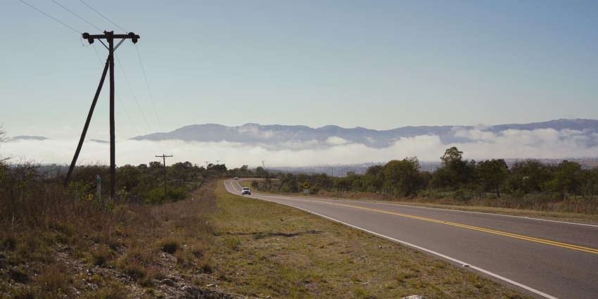 A far-off view of a car driving on a broad road leading surrounded by lush greenery.