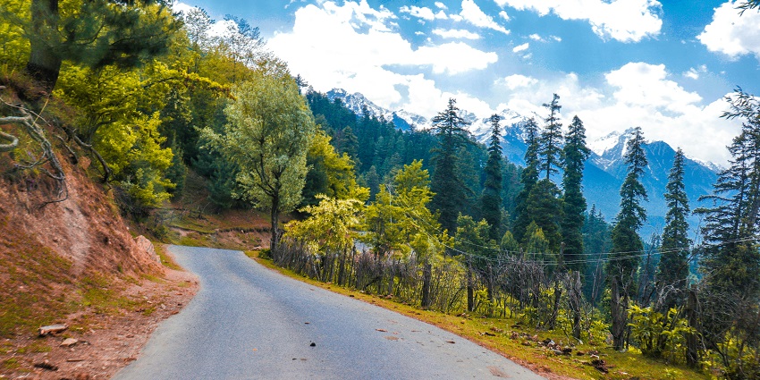 Scenic view of road with rocky mountains on one side and lush greenery on the other side.