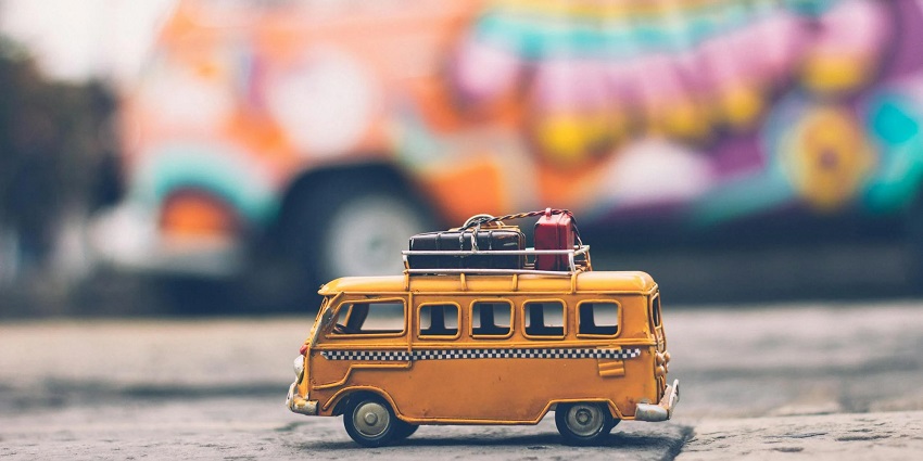 A miniature yellow-coloured bus carrying luggage on top of it with a colourful background.
