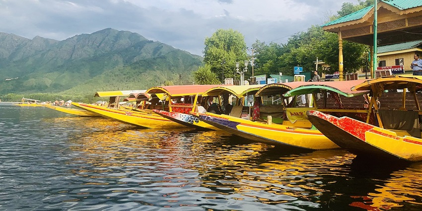 Traditional shikara boats gliding on Dal Lake at sunrise with snow‑capped peaks beyond