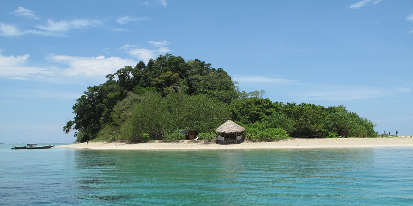 A small island with a mini hut in the middle of turquoise water on a sunny day.