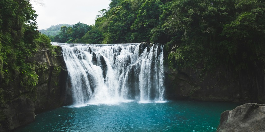 A majestic waterfall slowly cascading down into a scenic pool with turquoise waters and lush surroundings