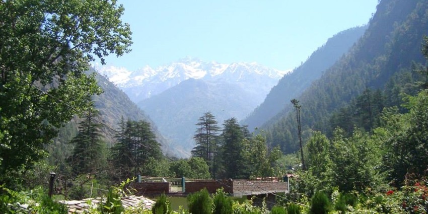 View of snow-capped Himalayan peaks and lush green valleys under a clear blue sky.