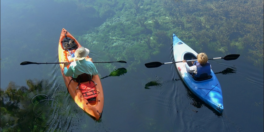 A view of an adult and a child kayaking in the middle of a turquoise body of water.