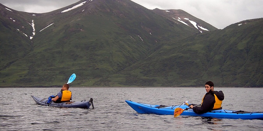 The view of travellers kayaking on a lake with towering mountains in the background