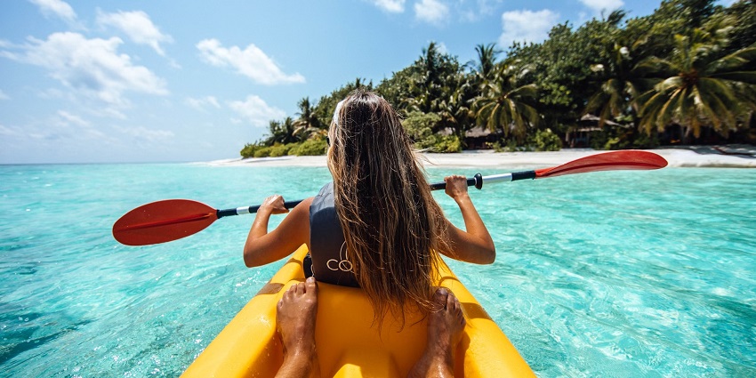 A woman on a yellow kayak with open hair and a paddle in her hands enjoying the views.