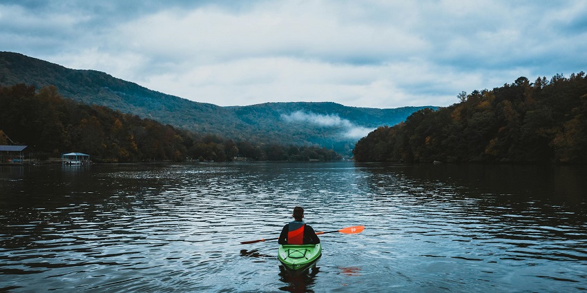A beautiful view of a man on a kayak on an ocean with mountains in the background.