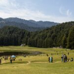 People on green grass fields during daytime in Khajjiar, enjoying their vacations.