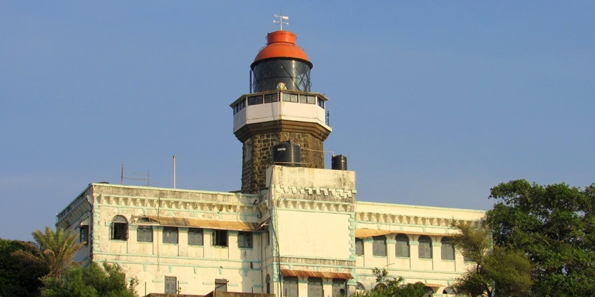 A picture of a lighthouse on the edge of a historical fort, surrounded by lush green forests