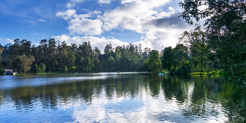 Scenic Kodaikanal Lake surrounded by lush hills, boats, and misty skies in Tamil Nadu.