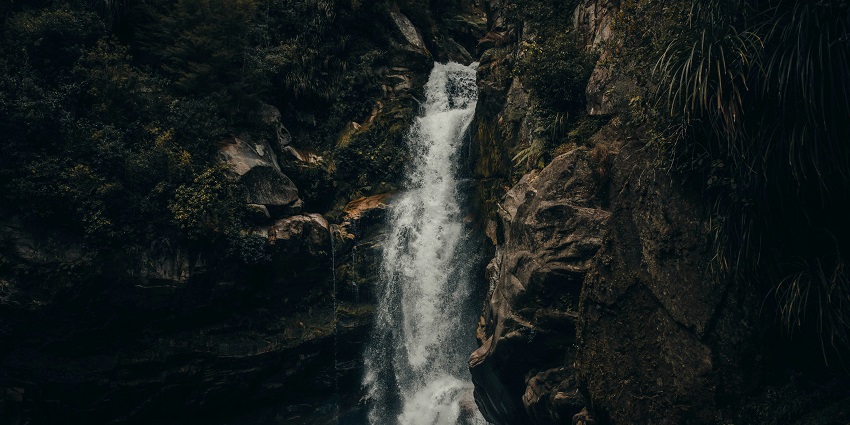 Scenic waterfall cascading down rocky cliffs, surrounded by lush green vegetation.