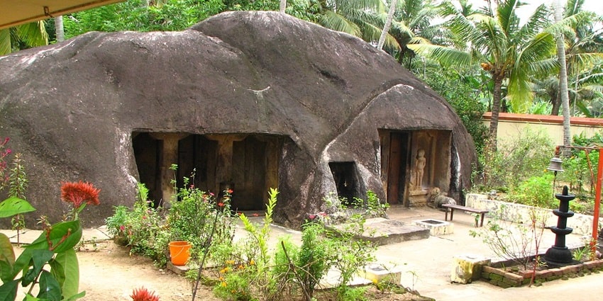 A view of Kottukkal Cave Temple in Kerala surrounded by lush green trees during the day.