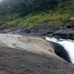 A breathtaking view of Kozhippara Falls flowing through a small rock amidst lush greenery.