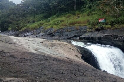 A breathtaking view of Kozhippara Falls flowing through a small rock amidst lush greenery.