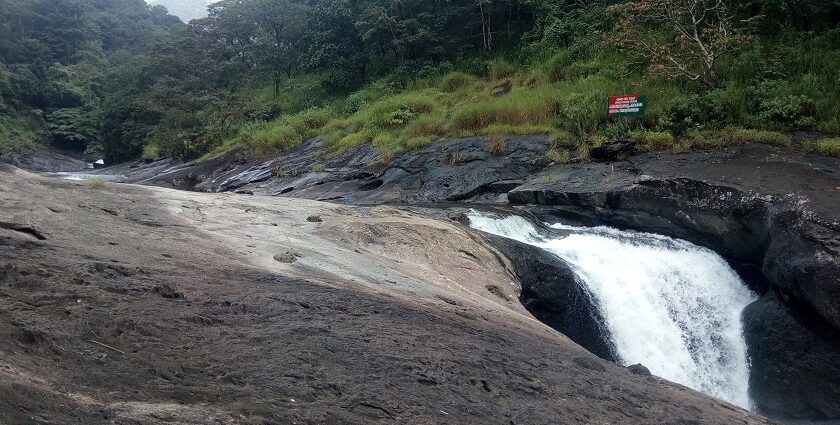 A breathtaking view of Kozhippara Falls flowing through a small rock amidst lush greenery.