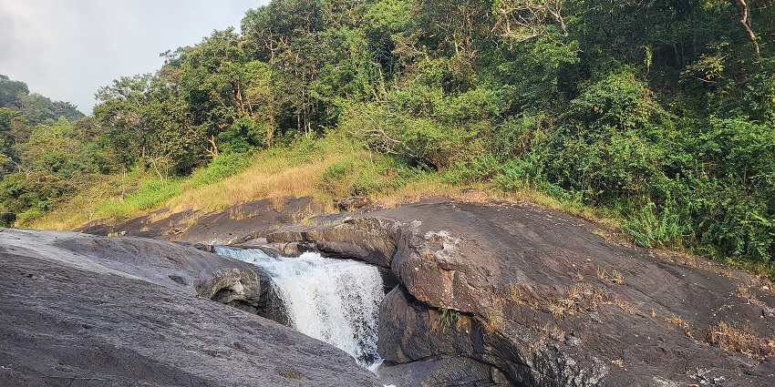 Picturesque Kozhippara Waterfalls, cascading over rocks surrounded by dense forest.