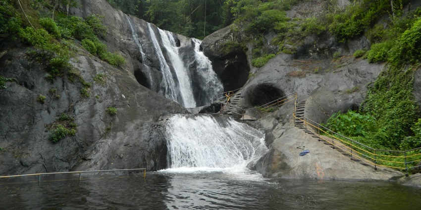 A scenic view of water falling off rocky cliffs at Kumbhavurutty Waterfalls in Kollam
