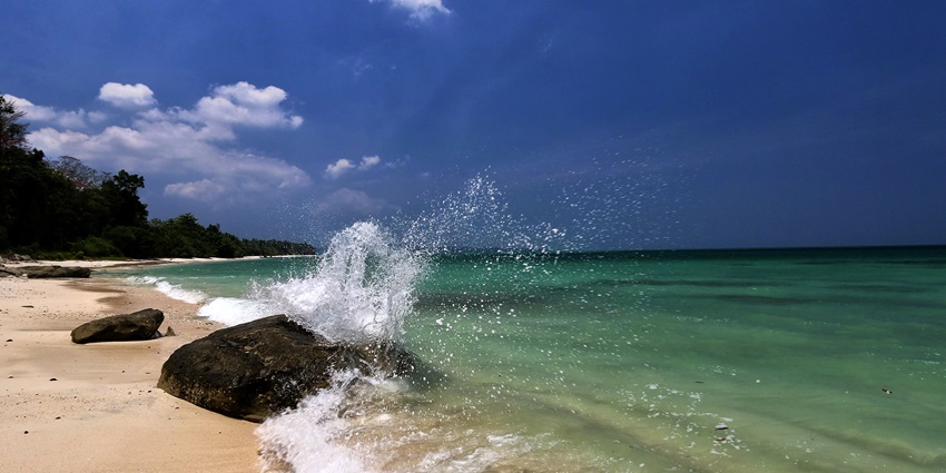 A beautiful view of a beach in Havelock Island where waves are crashing against a rock.