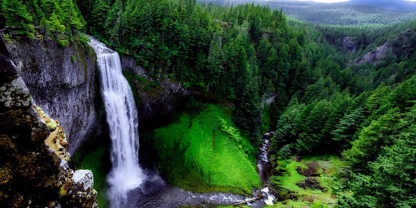 Stunning landscape photography of a waterfall surrounded by green forest and big rocks.