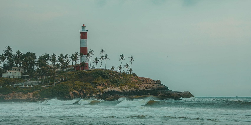 A scenic view of waves striking the rocky shore at Lighthouse Beach in Kovalam, Kerala