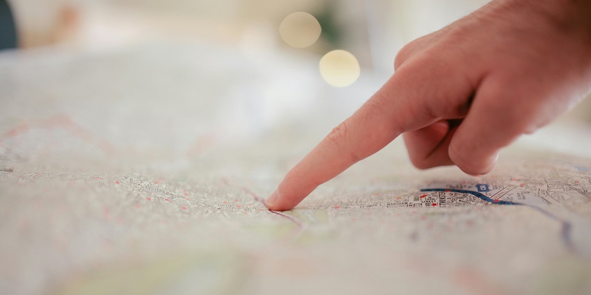 A focused shot of a person pointing at a location on a map on a table during the day.
