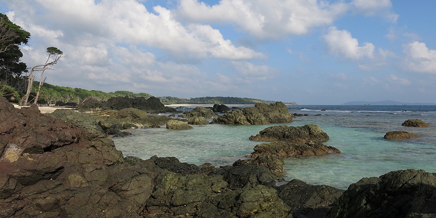 A beautiful view of the island with clear and calm water with rocks on the shore.