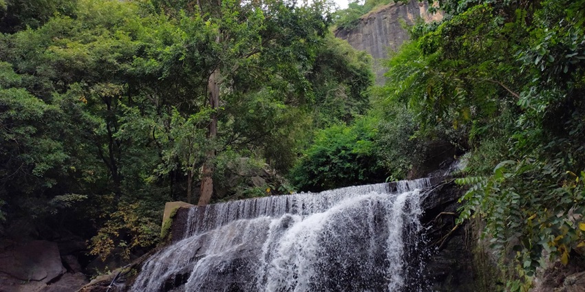 A stunning daytime view of a waterfall encircled by lush greenery and enormous rocks.