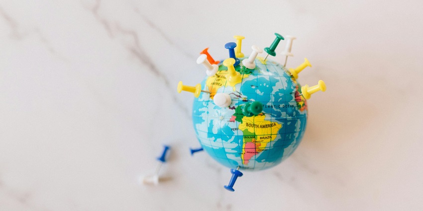 A view of a globe with colourful push pins on it, representing the location of a place.
