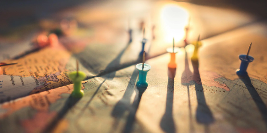 A close-up focused view of colourful push pins on a world map during the golden hour.