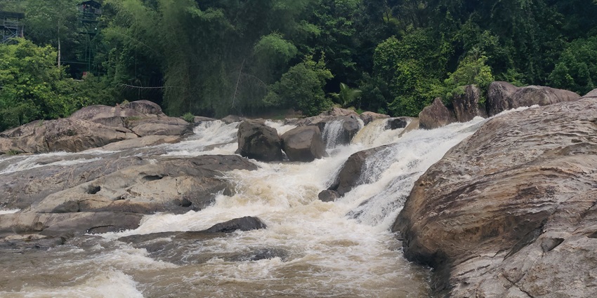 A stunning view of water flowing freely over small encircled by lush green trees.