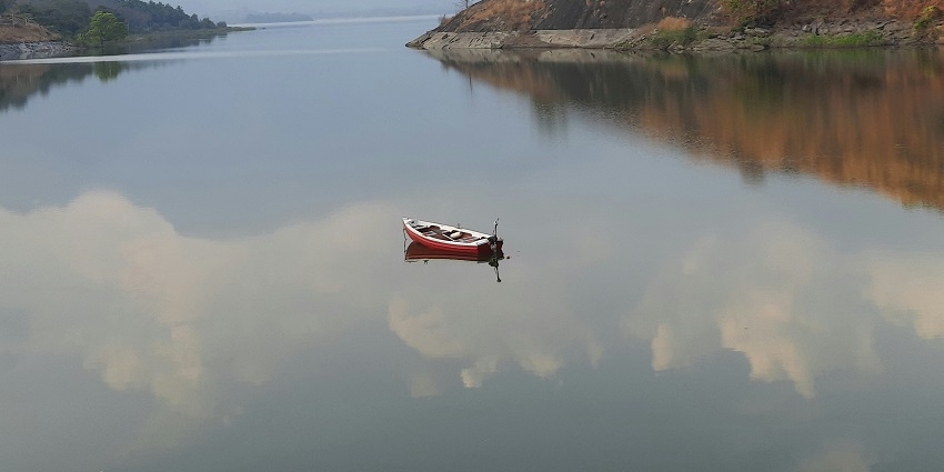 A stunning view of a red and white boat in the middle of a water body surrounded by hills.