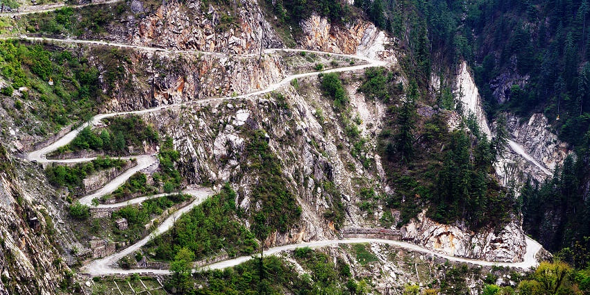 Road of Malana, snaking up a steep mountainside covered with trees and rocky terrain