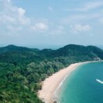 Mesmerising aerial view of a beach encircled by lush greenery during the day in Malaysia.