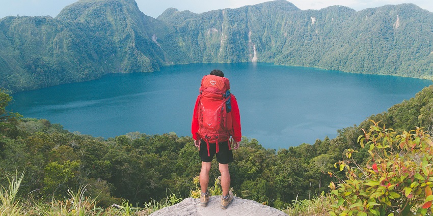 Photo of Hiker on Top of Rock Facing a Lake - pack the essential items for your journey