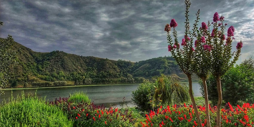 Manasbal Lake in Kashmir, showcasing calm waters, moored boats, and surrounding greenery