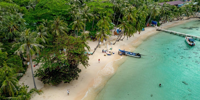 A stunning view of an island with clear turquoise waters and two blue and red boats in it.