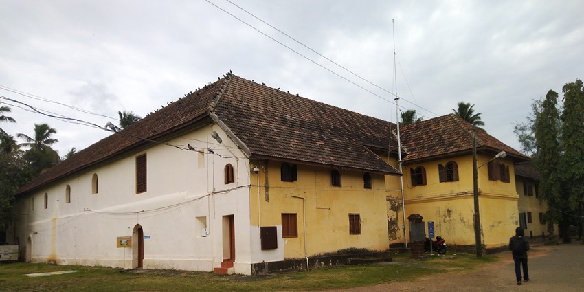 A front view of the Mattancherry Palace in Kochi with lush green trees around it.