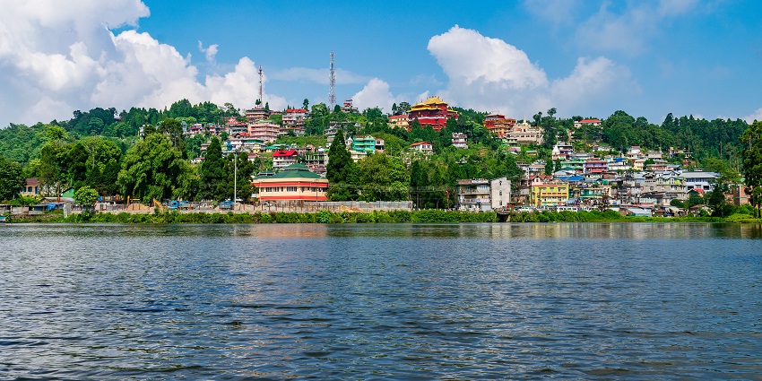 Tranquil view of Mirik Lake, surrounded by lush greenery and rolling hills and blue sky