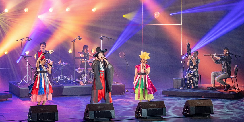 Musicians in traditional attire perform live on stage with vibrant lights and instruments.