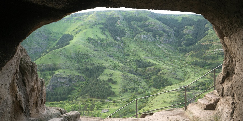 A view of the lush green valleys surrounding a cave on the mountains makes for a scenic sight