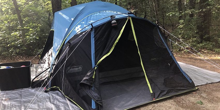 Camping tent pitched on blue tarp amid grassy terrain with gear scattered nearby