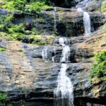 A breathtaking view of a waterfall in Munnar flowing through rocks surrounded by greenery.