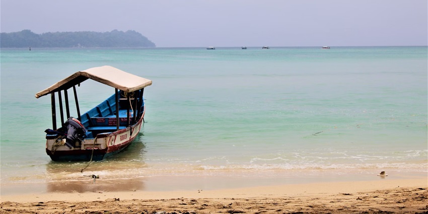 A boat lies on the shoreline of the Neil Island beach and the waters are clear and calm