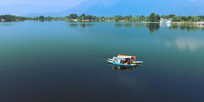 Shikara boat on tranquil Nigeen Lake with Mughal gardens in the backdrop