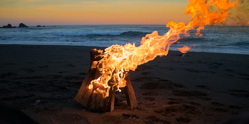 Cosy beach bonfire crackling at sunset, with flames against the backdrop of the sea