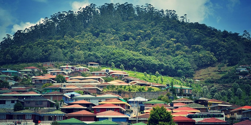 A breathtaking view of colourful houses on a hill in Ooty with lush greenery in the background